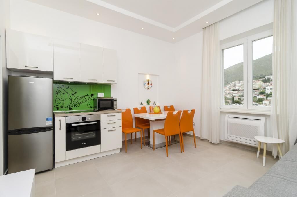 Una cucina moderna con mobili bianchi, una parete di sfondo verde e un'area pranzo con sedie arancioni.