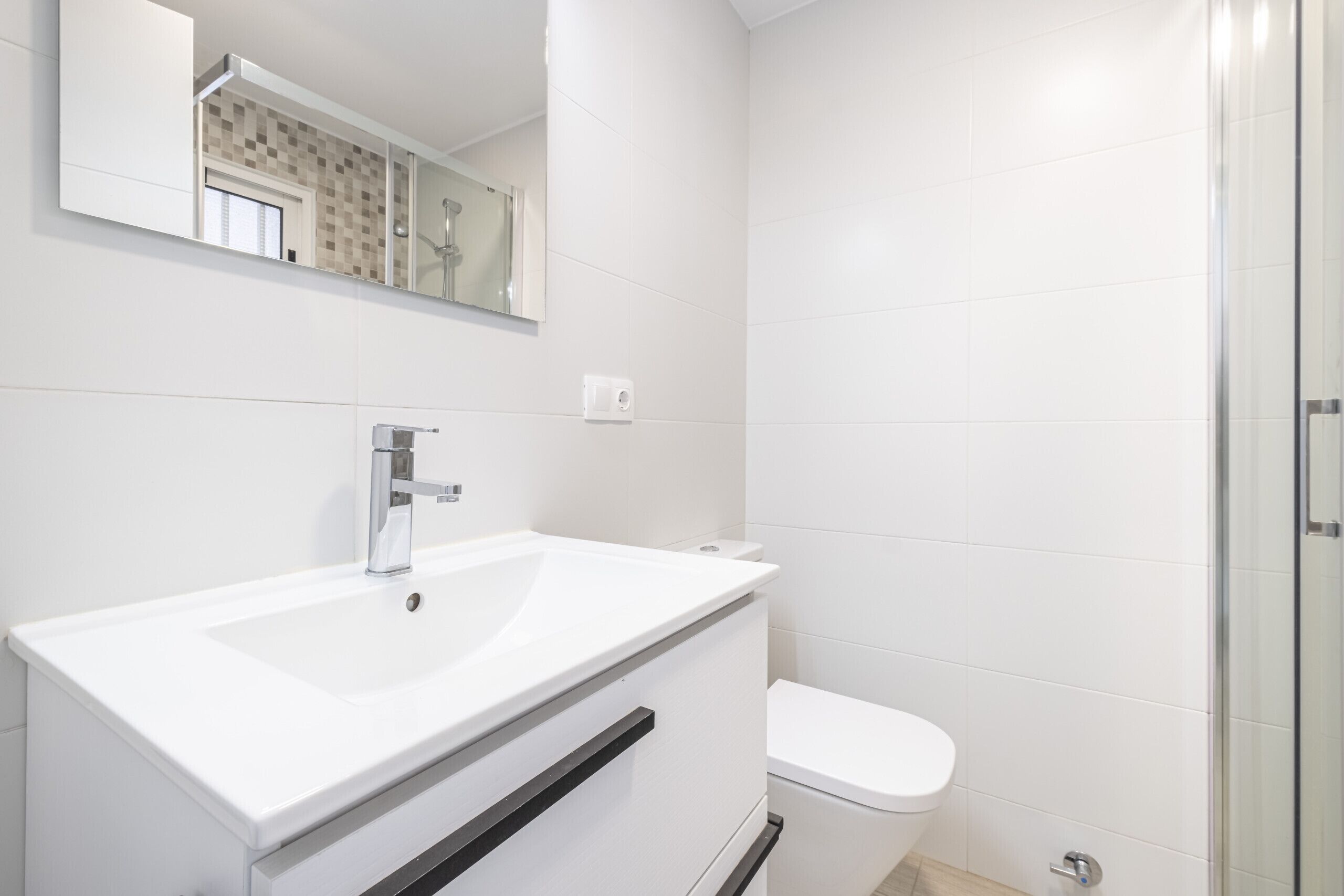 A modern bathroom with a white sink, a toilet, and a glass shower enclosure.
