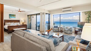 A spacious living room with a large window overlooking the ocean, a comfortable sofa, a wooden bed, and a television. - Stunning, Oceanfront Deluxe Penthouse with Island Views - Sands of Kahana 282 (Lahaina)