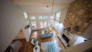 A spacious living area with a stone fireplace, wooden flooring, and a large window overlooking a deck. - 6000 SF Lakehouse with Hot Tub Games Dock and Ramp (Camden)