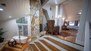 A spacious bathroom with a stone wall, a freestanding bathtub, and a wicker chair. - 6000 SF Lakehouse with Hot Tub Games Dock and Ramp (Camden)