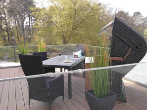 Ein Essbereich im Freien mit Tisch und Stühlen, umgeben von Topfpflanzen und Blick auf Bäume.
