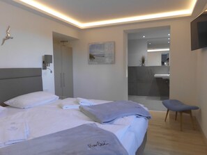 Ein modernes Hotelzimmer mit einem großen Bett, einer kleinen Sitzecke, einem Badezimmer mit Spiegel und einem Bild an der Wand.
