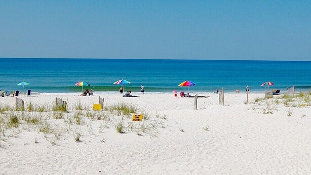 A beach with white sand, clear blue water, and colorful umbrellas.