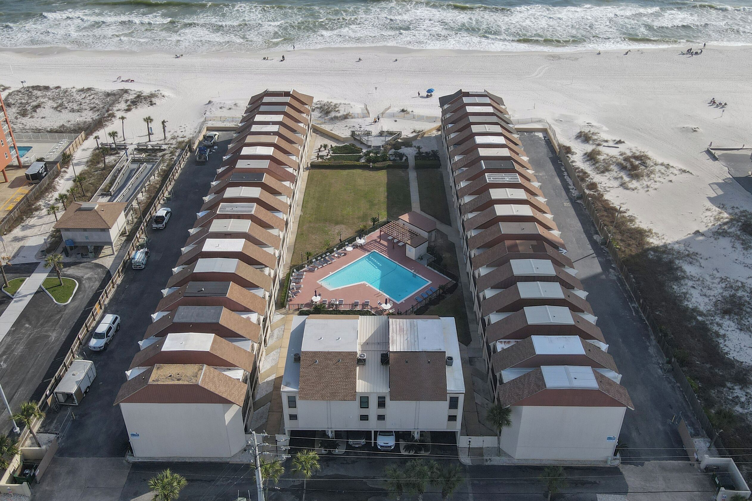 Um hotel à beira-mar com piscina central, várias varandas e área de estacionamento.