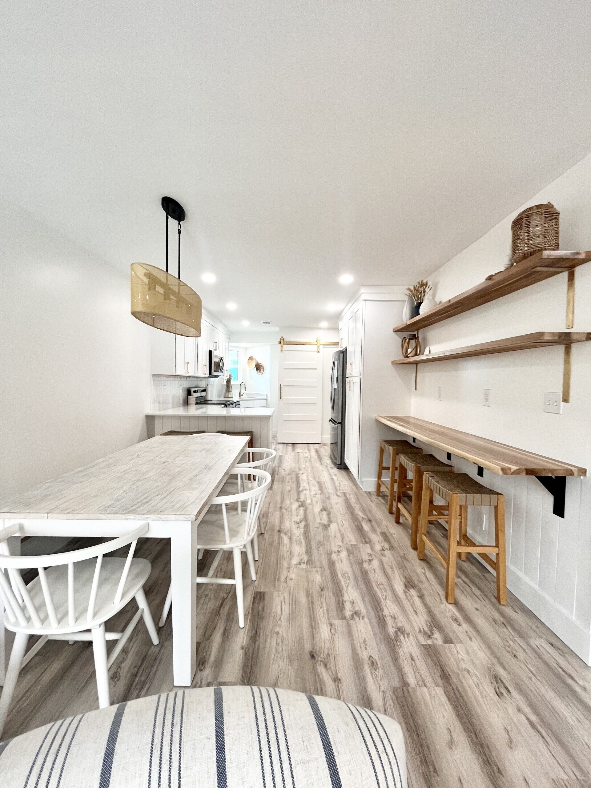 A modern kitchen with white cabinetry, a wooden dining table with white chairs, and wooden bar stools.