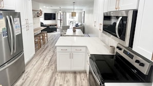 A modern kitchen with white cabinets, stainless steel appliances, and a wooden floor.