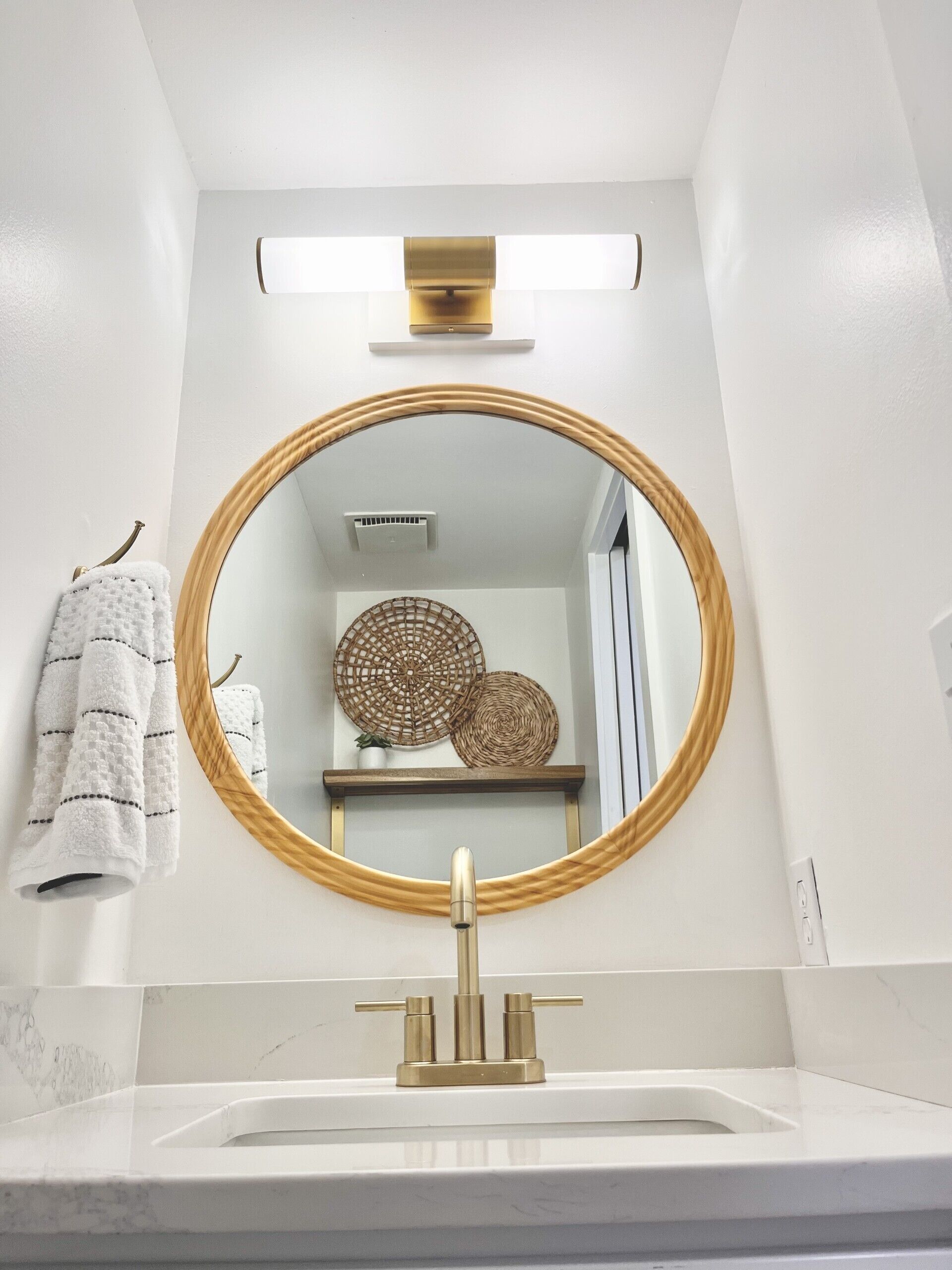 A bathroom with a round mirror, a gold faucet, and a towel hanging on a hook.