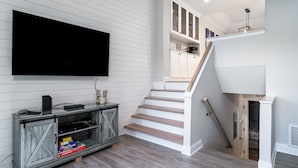 Una sala de estar moderna con televisor de pantalla plana, piso de madera y una escalera que conduce a una zona en altura.