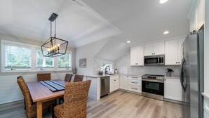 Una cocina moderna con armarios blancos, electrodomésticos de acero inoxidable y un comedor con sillas de mimbre y una mesa de madera.