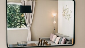 Ett modernt vardagsrum med en soffa, ett sidobord, en lampa och utsikt över grönområden utanför.