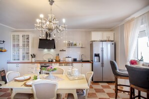 A kitchen with white cabinets, a stainless steel refrigerator, a chandelier, and a dining area with a table set for four.