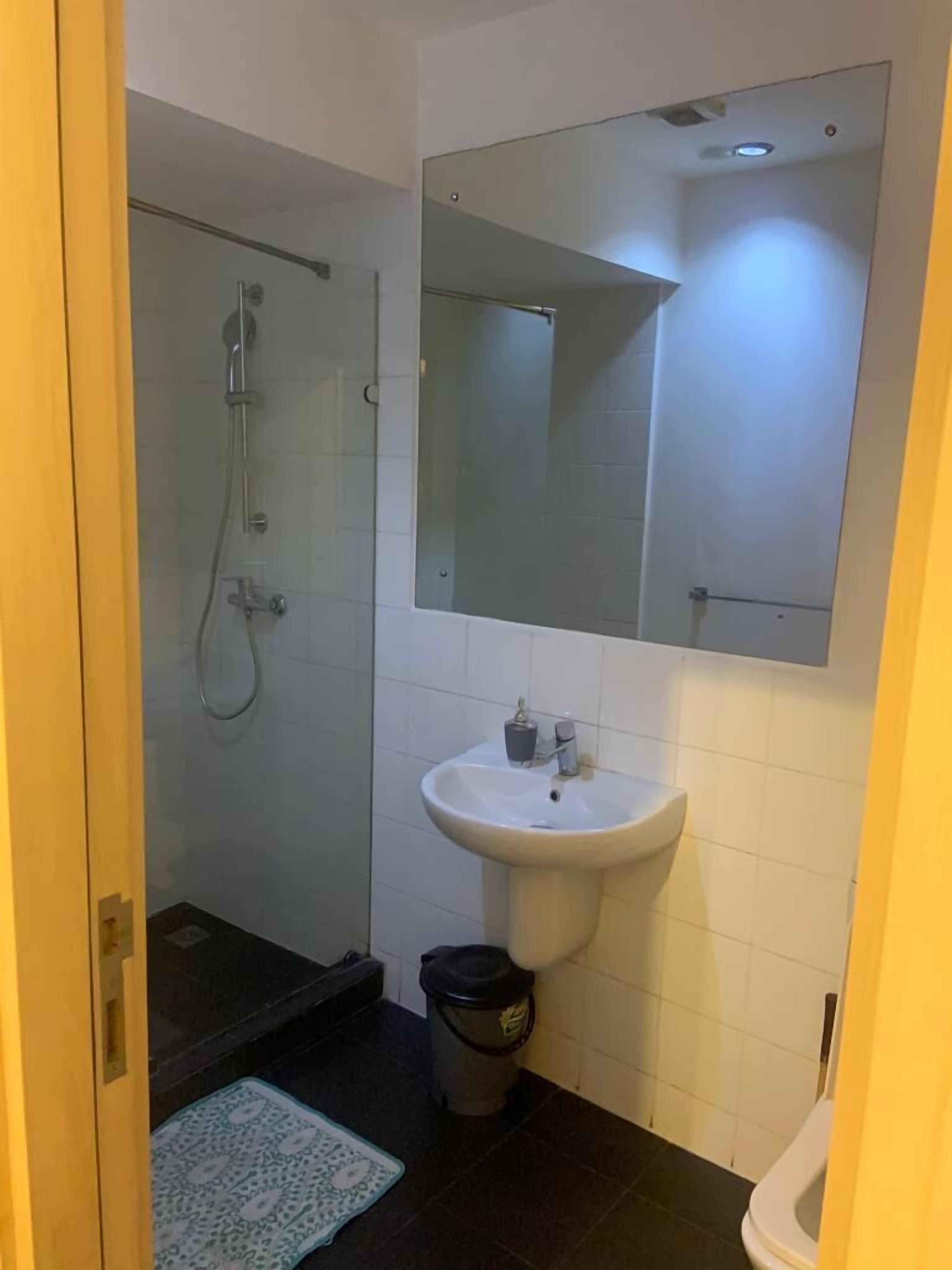 A bathroom with a glass shower enclosure, a white sink with a mirror above it, and a small trash bin.