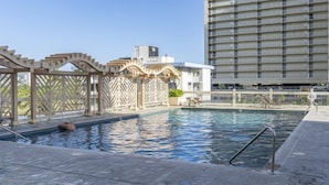 A rooftop pool with a pergola, a lounge chair, and a high-rise building in the background.