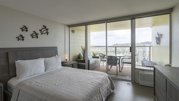 A modern hotel room with a large bed, a balcony with a view of the city, and a small seating area.