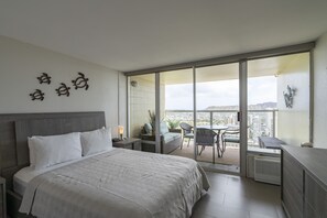 Une chambre d’hôtel moderne dotée d’un grand lit, d’un balcon offrant une vue sur la ville et d’un petit coin salon.