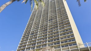 A tall hotel with a grid of balconies, a clear blue sky, and palm trees.