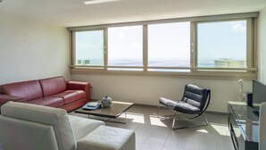 A modern living room with a red leather sofa, a white armchair, a black leather chair, a glass coffee table, and a TV on a stand.