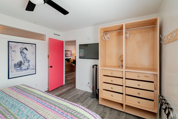Un dormitorio con una cama, una puerta rosa, un armario de madera, un televisor y un radiador.
