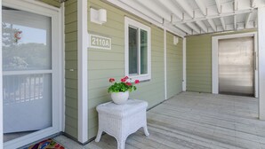 Eine überdachte Veranda mit einem weißen Korbtisch, auf dem ein Blumentopf steht, eine grüne Tür und ein Fenster mit einer Nummer.