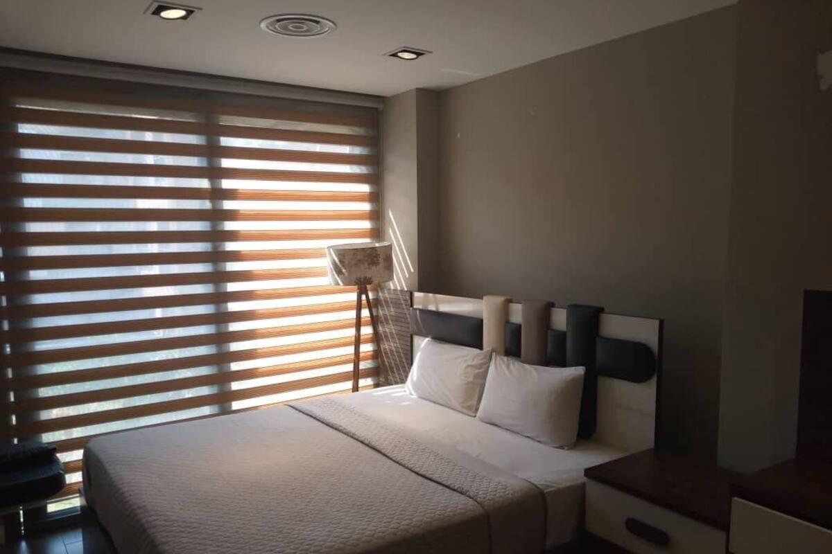 A bedroom with a bed, bedside tables, a desk, and a window with blinds.