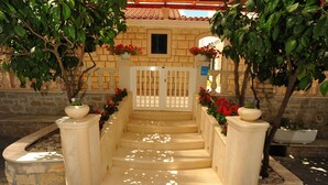 Un escalier en pierre mène à une entrée fermée par un portail, qui est entourée de plantes et de fleurs en pot.