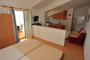 A compact living space with a kitchenette, a sofa, a dining area, and a sliding door leading to an outdoor patio. - Villa Anni (Sutivan)