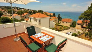 Un balcon avec une table et des chaises, donnant sur une ville côtière avec ses maisons et la mer.