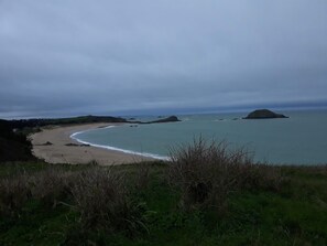 A coastal landscape with a sandy beach, calm sea, and distant hills.