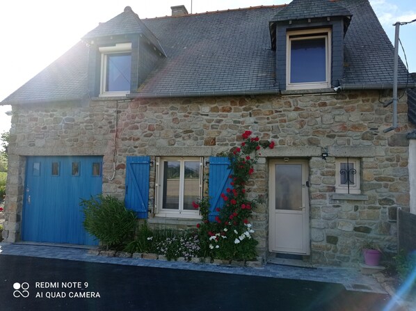 A stone house with a blue door, a blue shutter, and a small window with a white door.