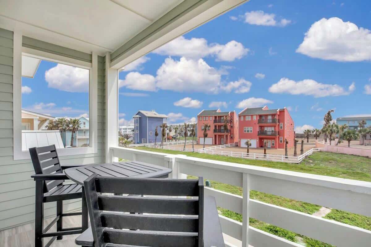 A balcony with a table and chairs, overlooking a residential area with colorful buildings and a clear sky.