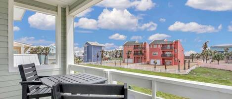 A balcony with a table and chairs, overlooking a residential area with colorful buildings and a clear sky.