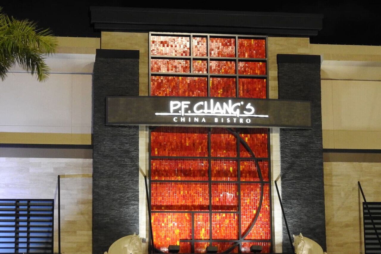 Het exterieur van P.F. Chang's China Bistro, met een opvallend verlicht bord en een decoratieve glazen gevel.