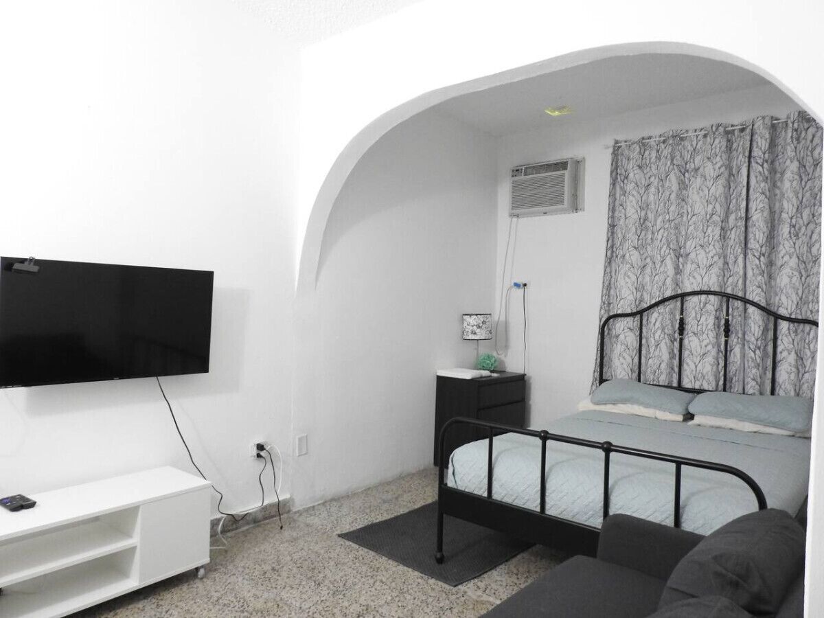 A bedroom with a bed, a TV, a bedside table, and a window with curtains.