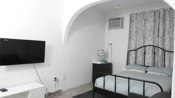 A bedroom with a bed, a TV, a bedside table, and a window with curtains.