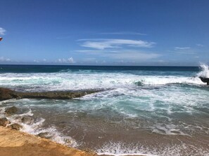 Una playa con olas rompiendo en la orilla, cielos despejados y un horizonte lejano.