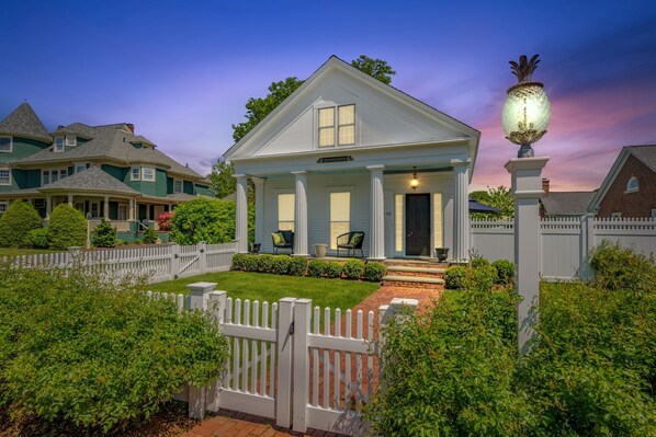 A two-story house with a porch, a white picket fence, and a well-maintained lawn.