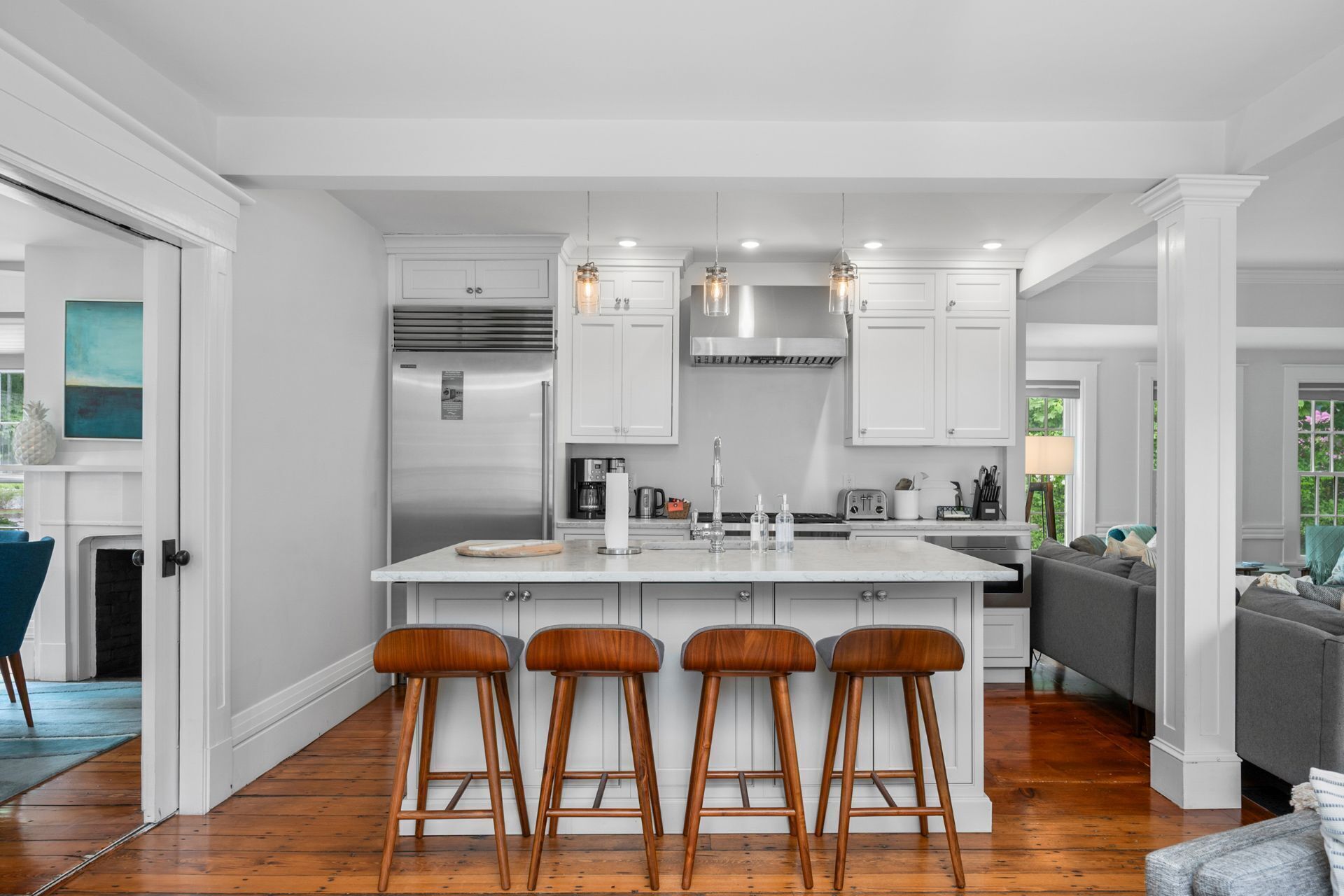 A modern kitchen with white cabinetry, a central island with stools, stainless steel appliances, and pendant lighting.