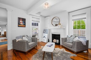A spacious living room with two grey sofas, a white fireplace, and a large window offering a view of greenery.