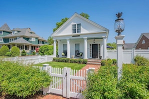 A white two-story house with a porch, a picket fence, and a well-maintained lawn.