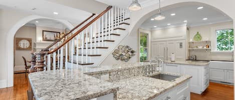 Una cocina amplia con encimera de mármol, armarios blancos y una escalera de madera.
