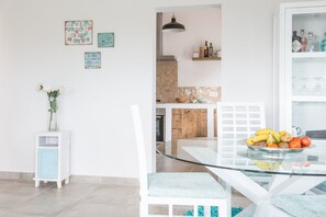 A modern kitchen with a glass dining table, white chairs, and a variety of kitchen appliances.