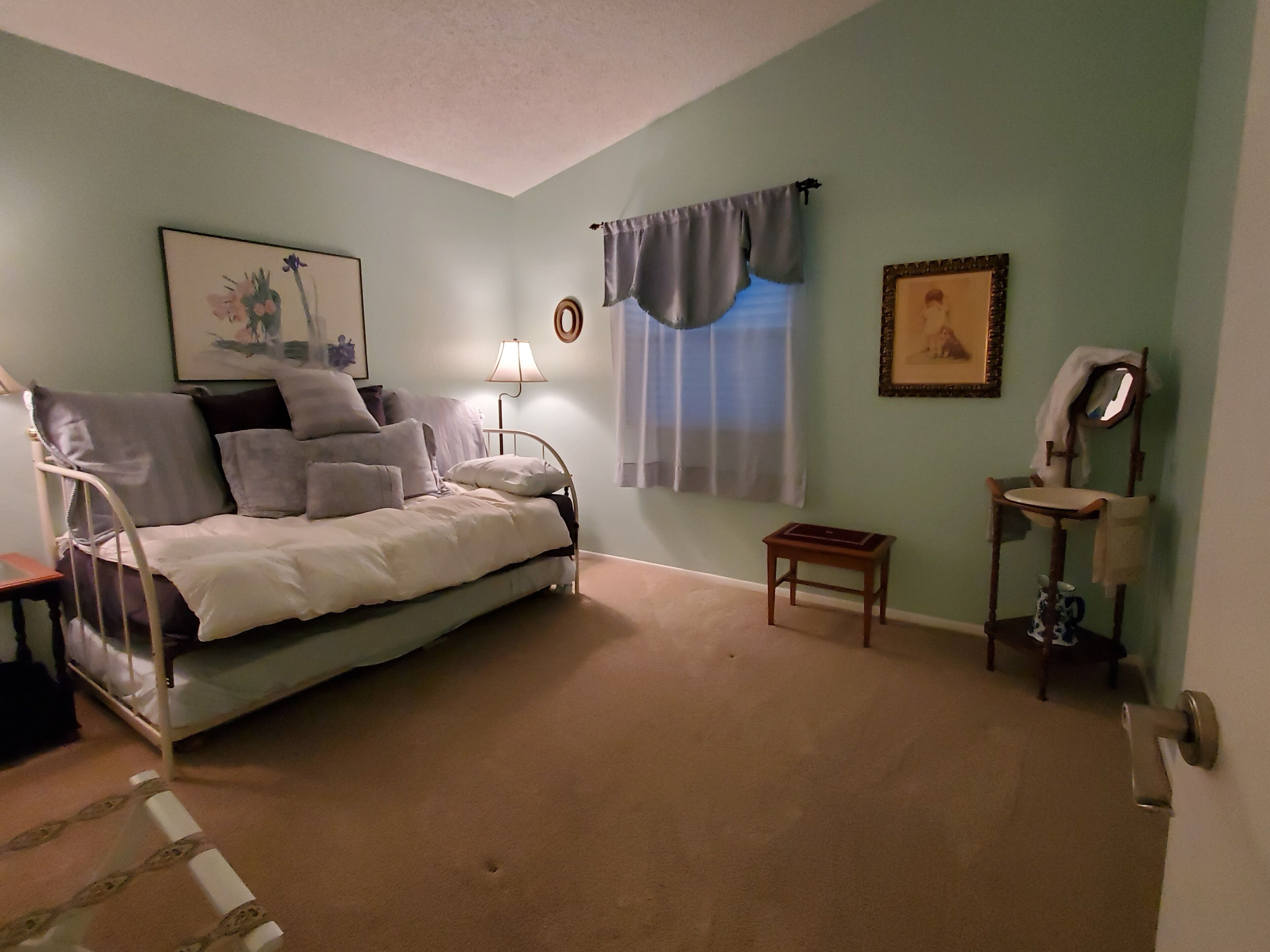 A bedroom with a bed, bedside table, lamp, and a small stool.