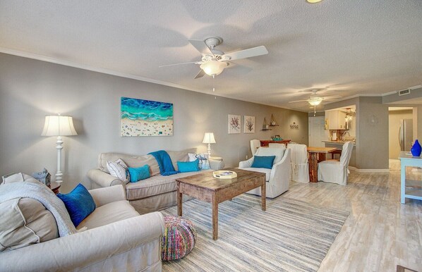 A spacious living room with a sofa, armchairs, a coffee table, and a ceiling fan.