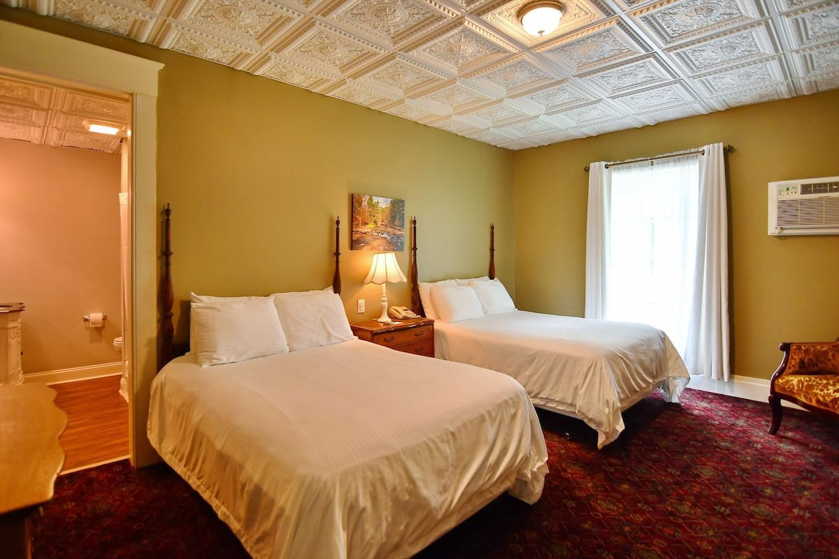 Une chambre d’hôtel avec deux lits, un tableau au mur, une lampe et une fenêtre avec des rideaux.