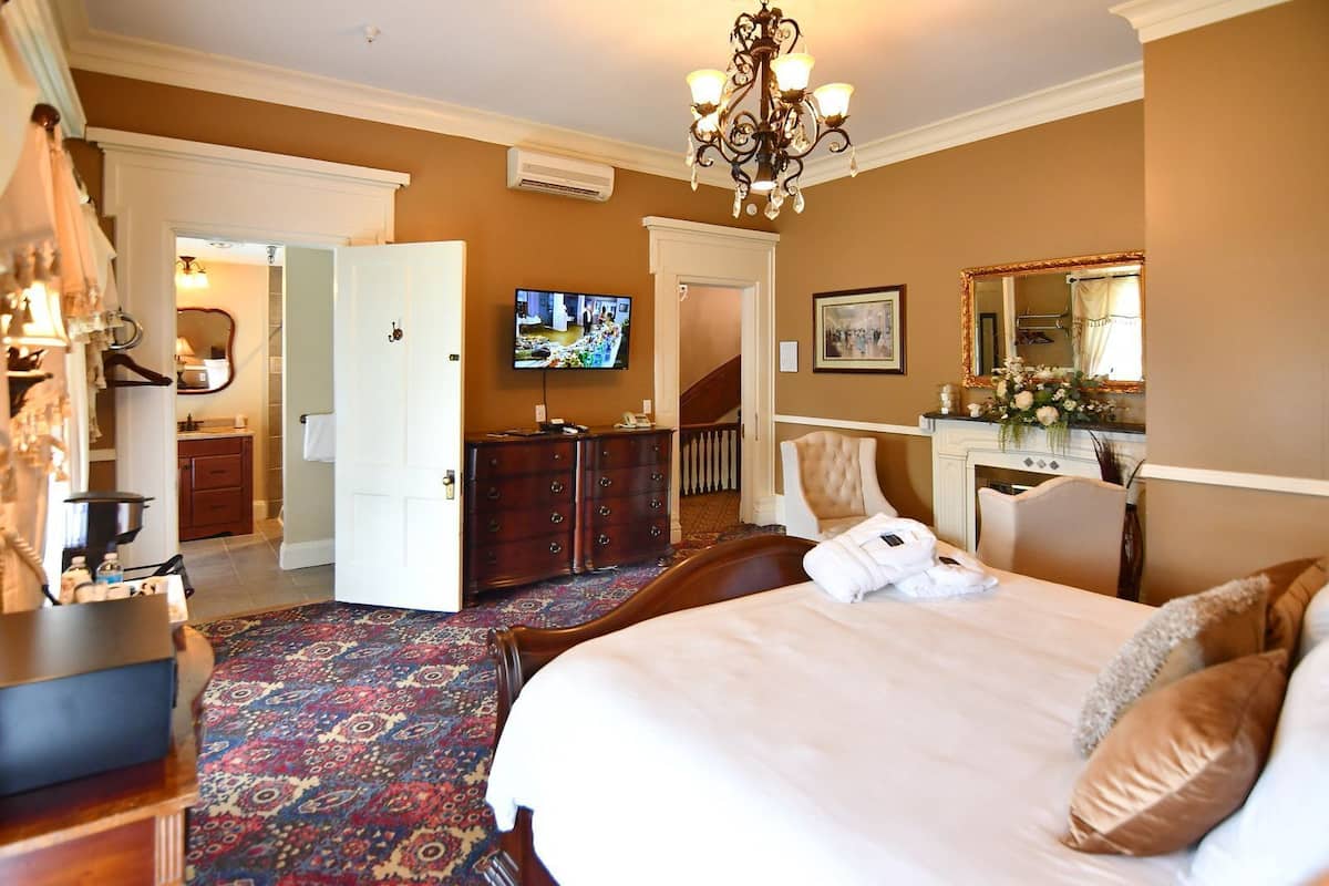 Une chambre d’hôtel avec un grand lit, une télévision, une commode, une chaise et un sol recouvert de moquette.