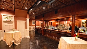 Angolo bar con pannelli in legno, bancone e due tavoli decorati con fiori.