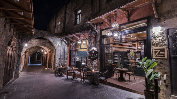 Una calle estrecha con un café que ofrece mesas al aire libre y un arco de piedra.