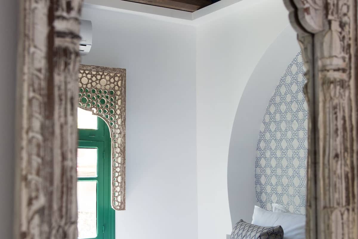 Een slaapkamer met een bed, een groen raam en een decoratieve spiegel.