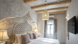 Un dormitorio con dos camas, un cabecero decorativo, una lámpara colgante, un teléfono en la mesita de noche y un televisor montado en la pared.